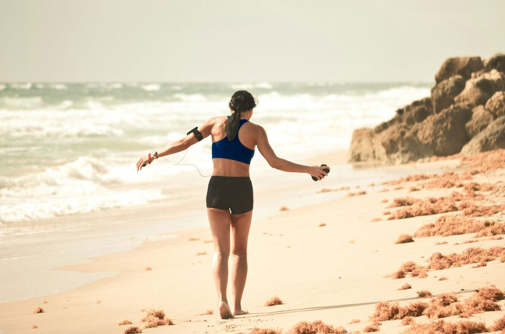 santé des femmes, femme sur la plage en tenue de sport écoutant de la musique